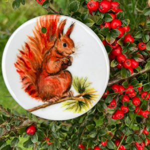 a photo of a 7cm diameter white glazed ceramic pendant printed with a red squirrel design.